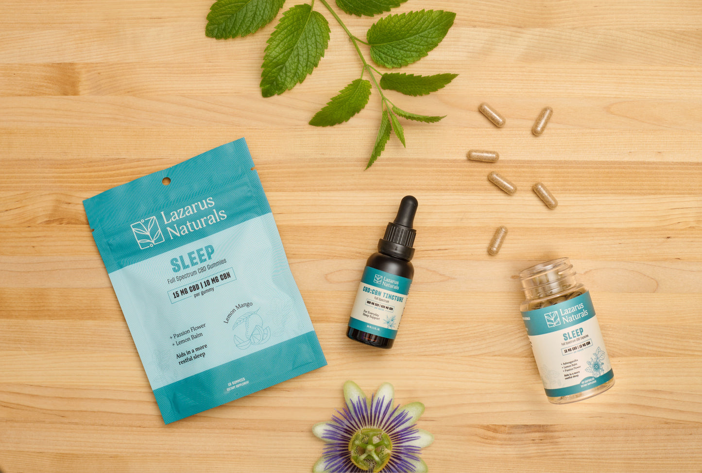 Lazarus Naturals Sleep gummies laid next to Lazarus Naturals CBD:CBN Sleep Tincture, and Lazarus Naturals Sleep Capsules with passionflower and lemon balm scattered around. 